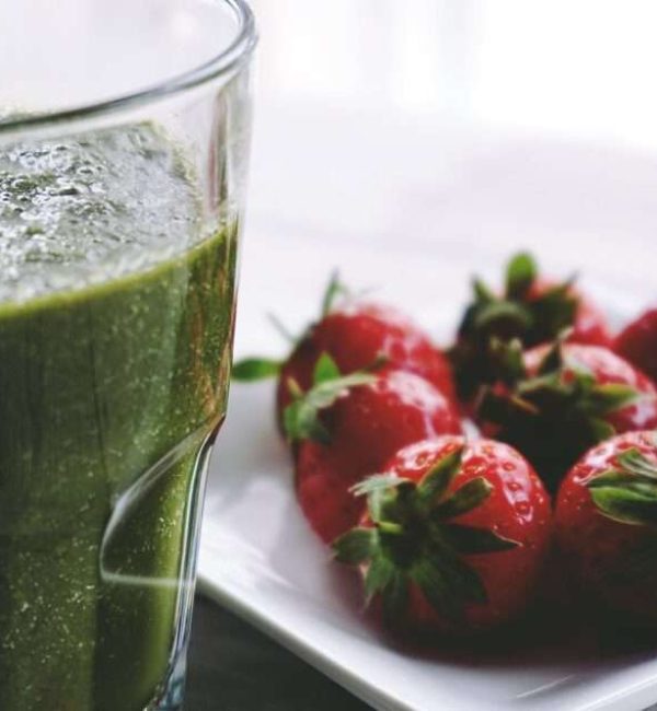 A plate of green juice shake and a plate of strawberries